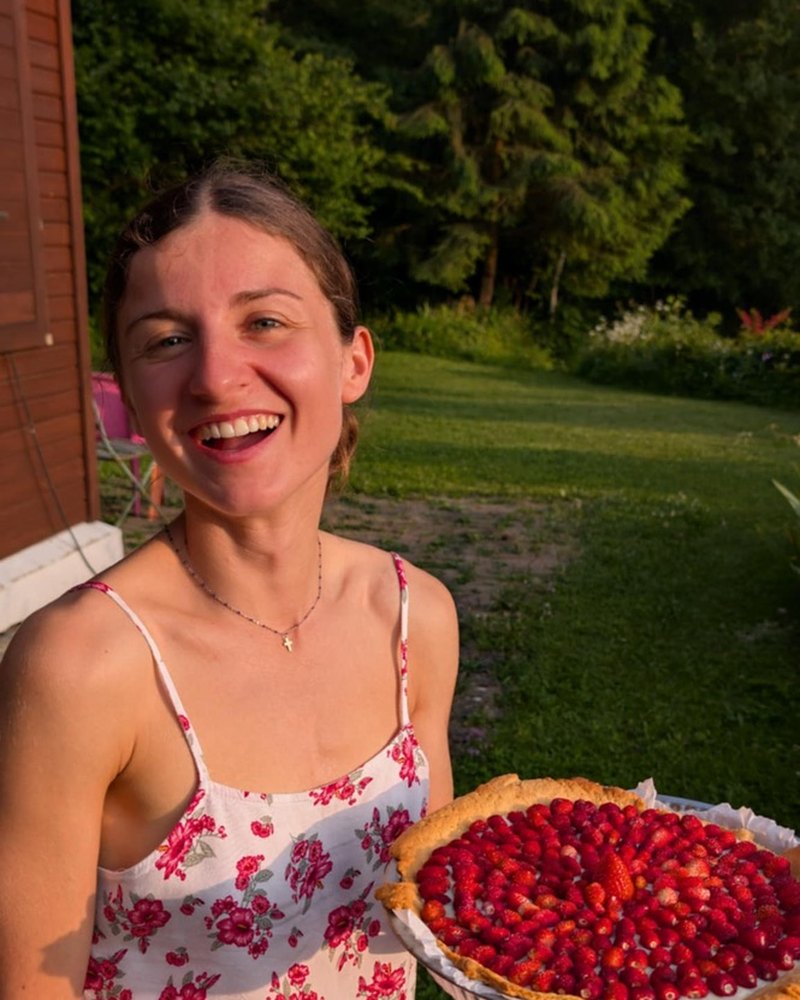 Oriane, souriante, tient une tarte aux fraises des bois dans un jardin